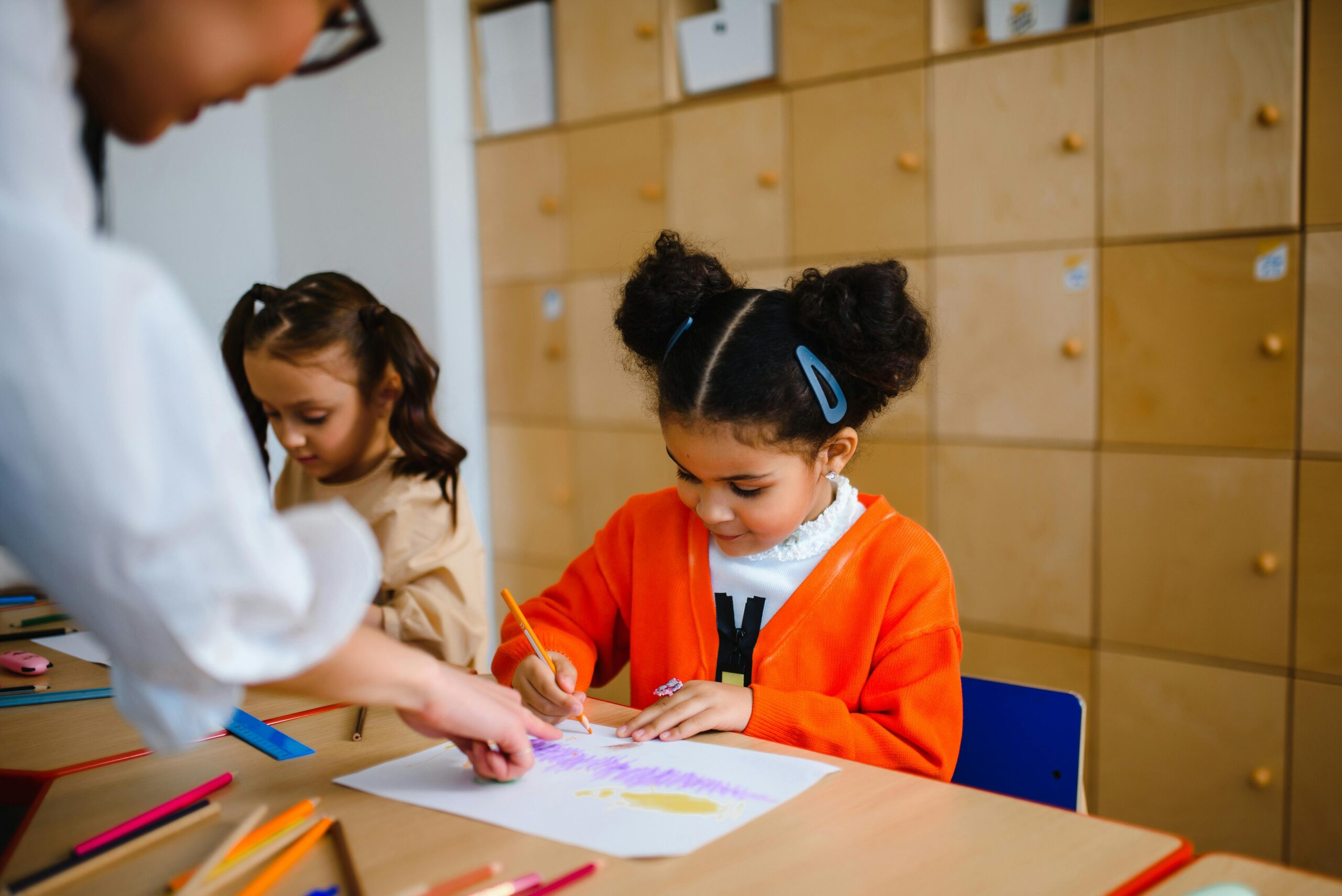 Children engage in creative drawing activities with teacher assistance in a vibrant classroom setting.